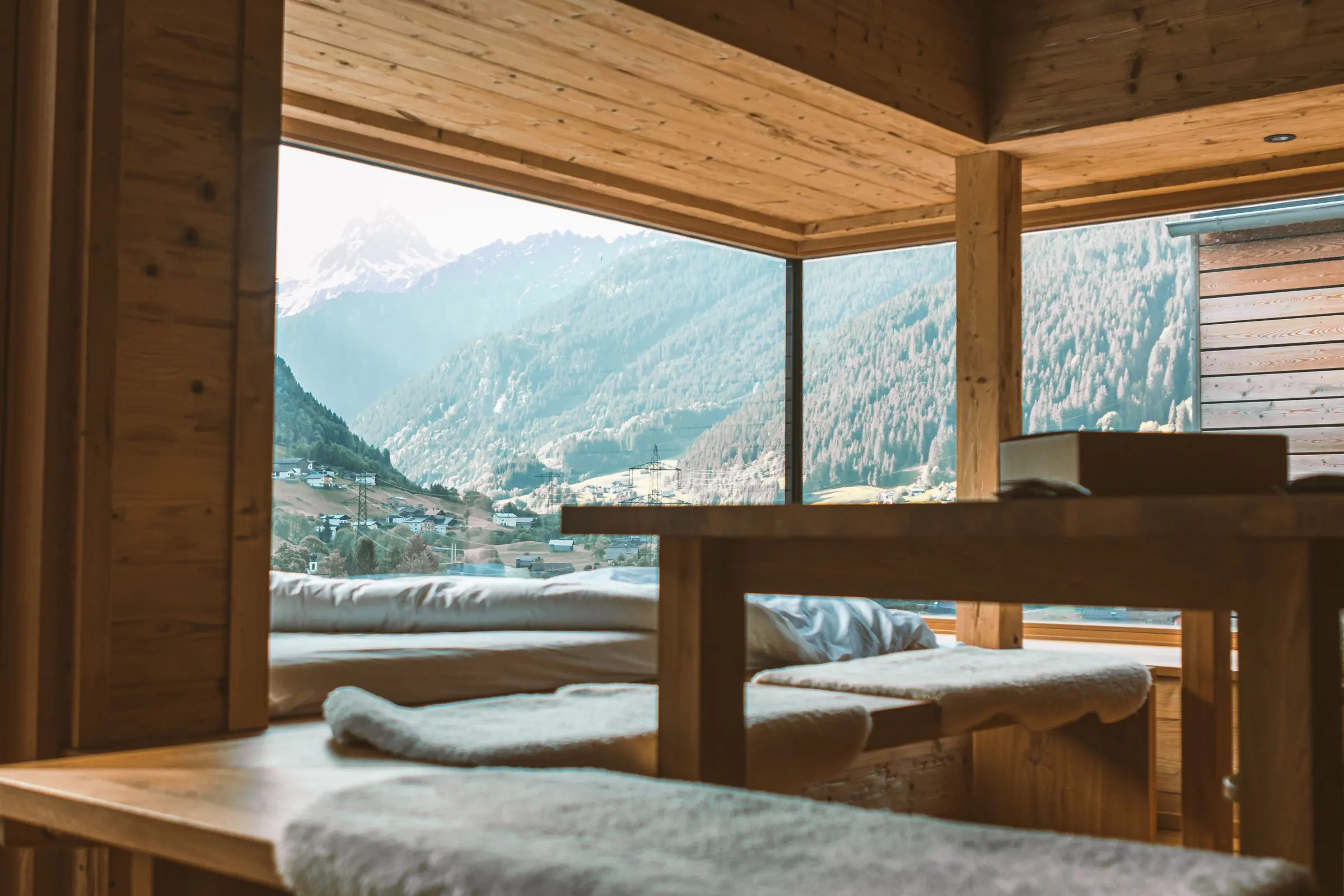Angolo in legno con panca, tavolo e grande vetrata aperta sulla valle e sulle montagne