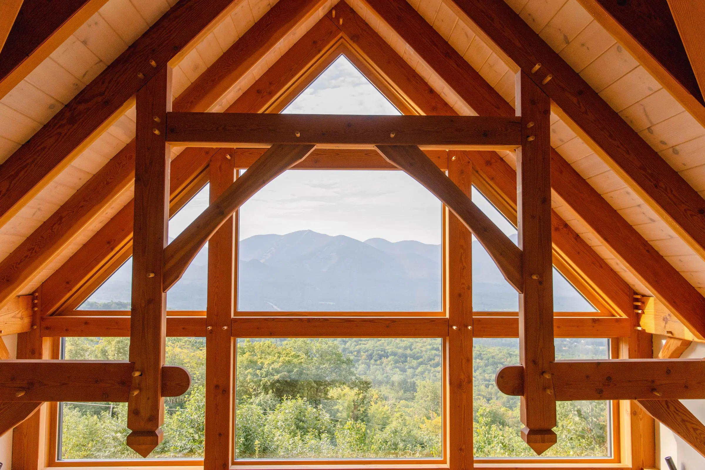 Interno sotto il tetto con capriate in legno e vetrata triangolare sulle montagne