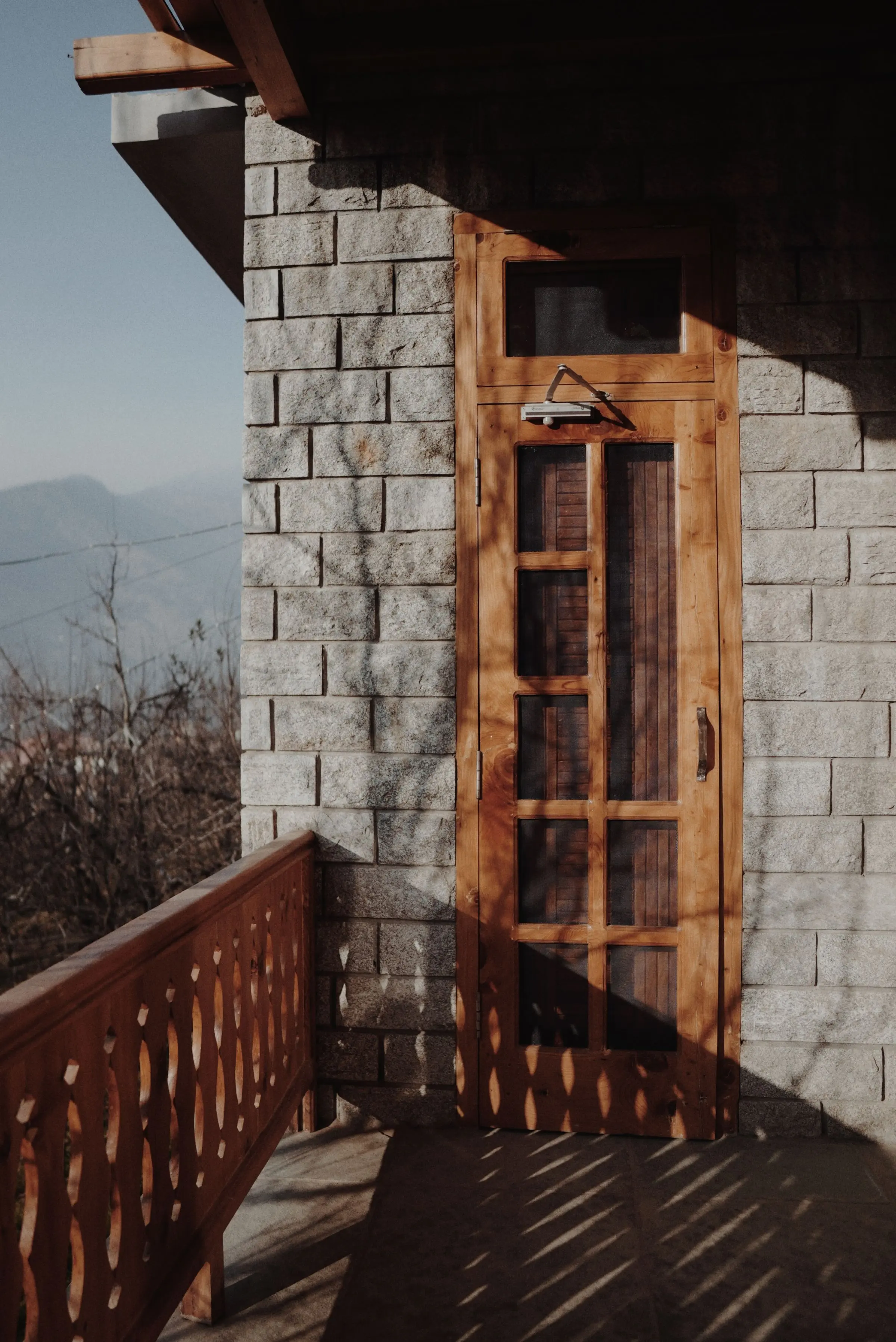 Muro in pietra squadrata con porta in legno e balcone in legno, valle nella nebbia