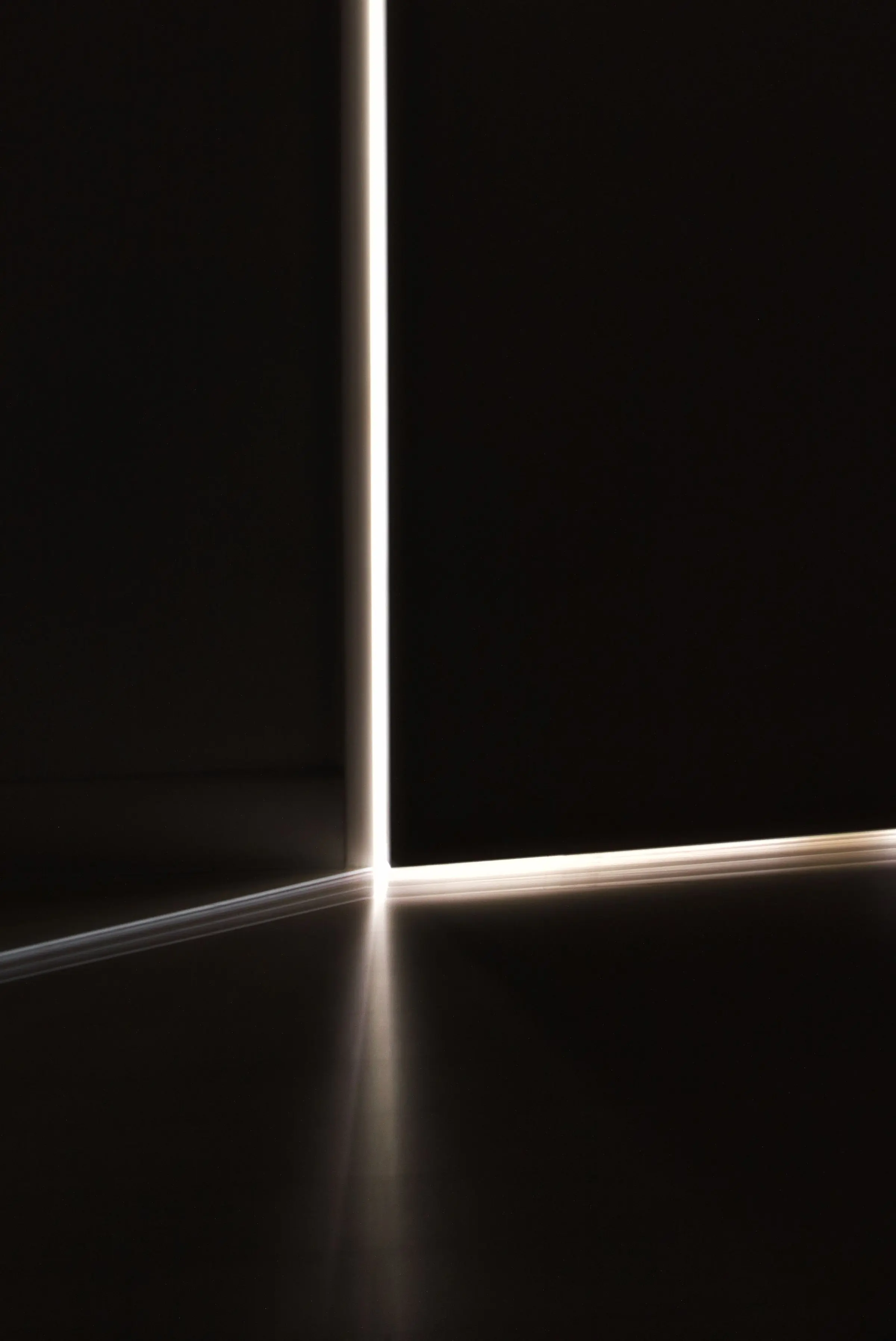 Una lama di luce verticale tra due pareti scure che si allunga sul pavimento
