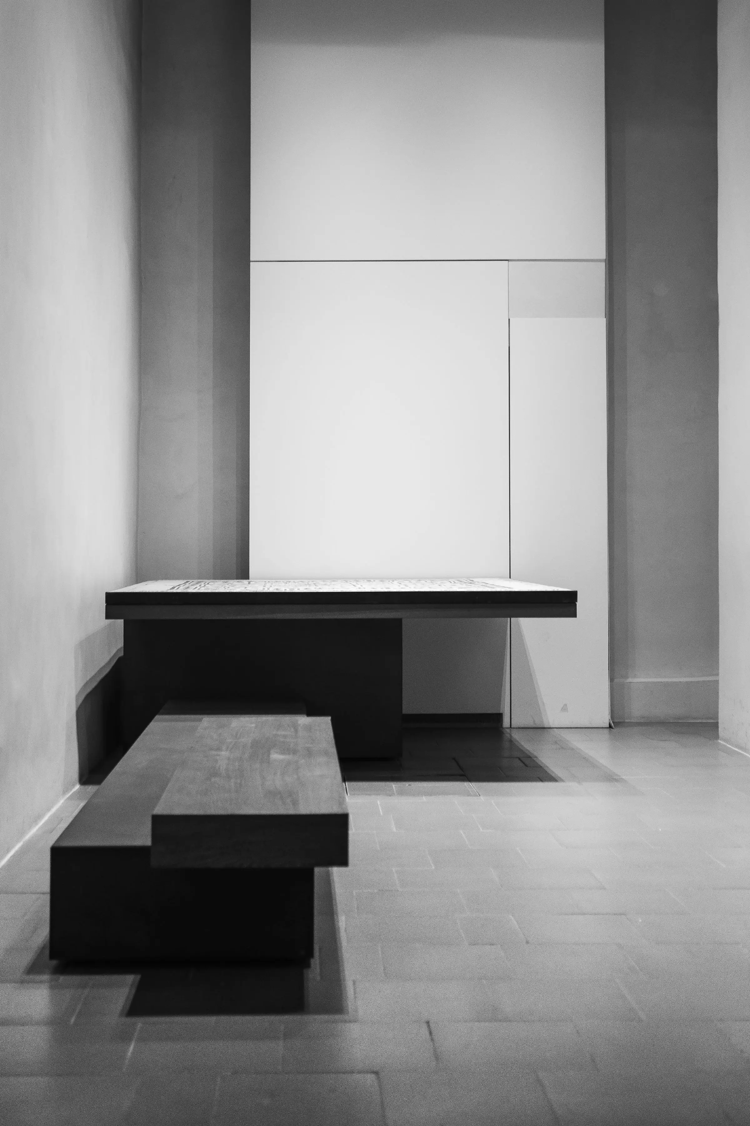 Interno in bianco e nero con una panca e un tavolino bassi davanti a pareti a riquadri