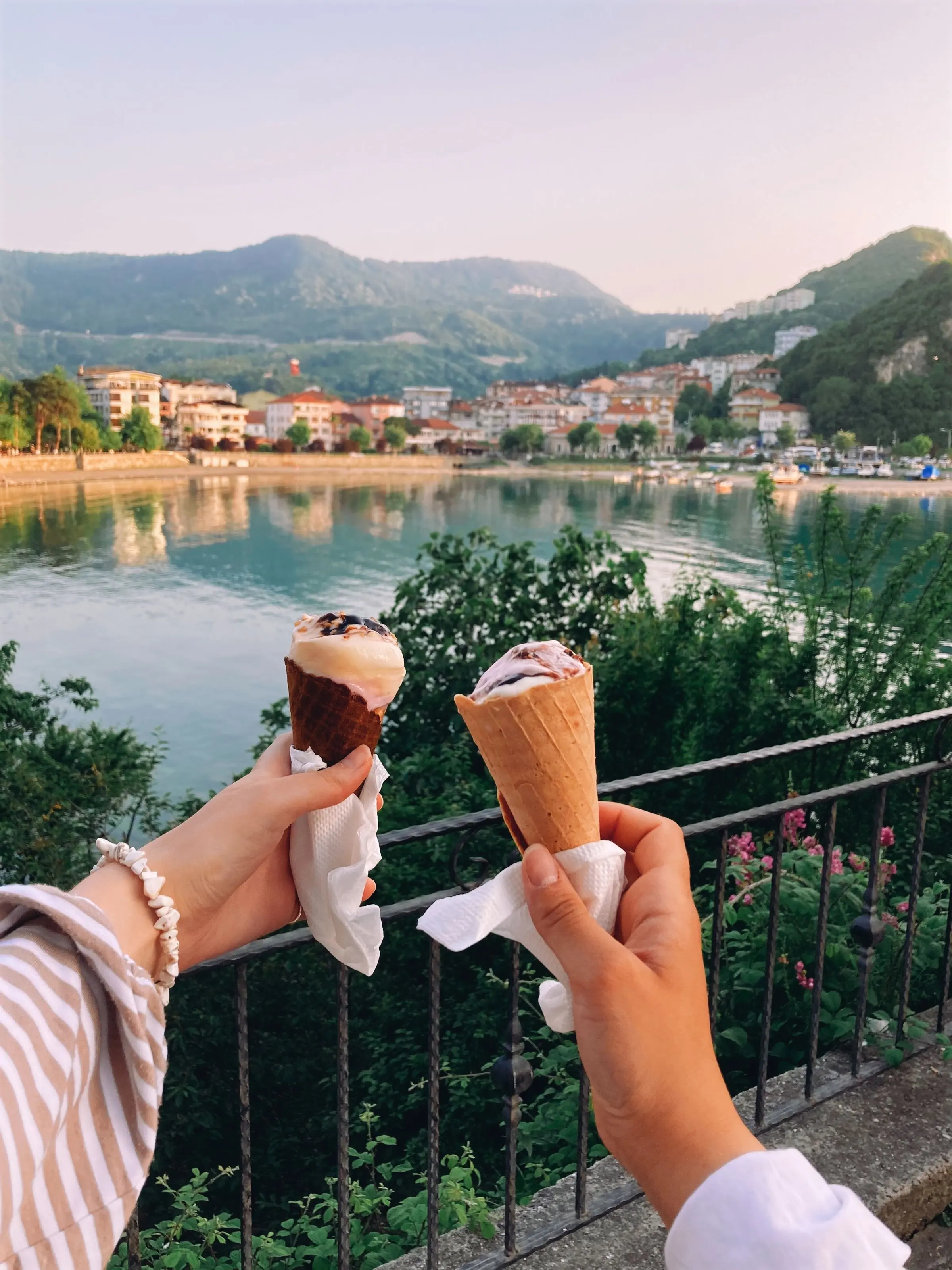 Due mani tengono due coni gelato davanti al lago, con il paese e i monti sullo sfondo