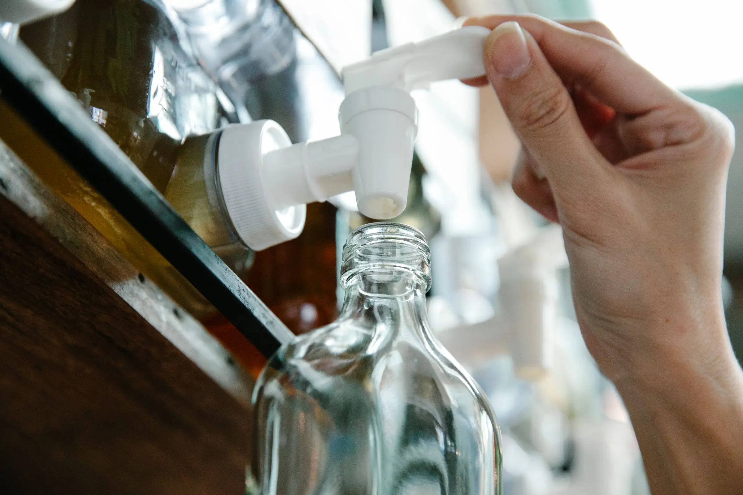 Una mano apre il rubinetto del dispenser e riempie una bottiglia di vetro