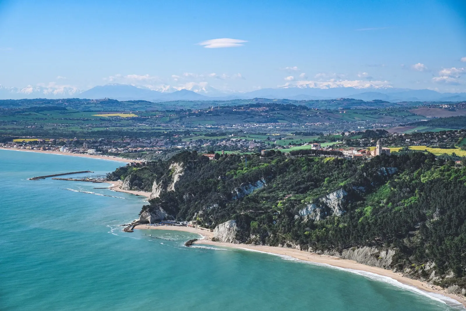 Costa dall'alto: un promontorio verde, la spiaggia e il mare turchese, i monti sullo sfondo