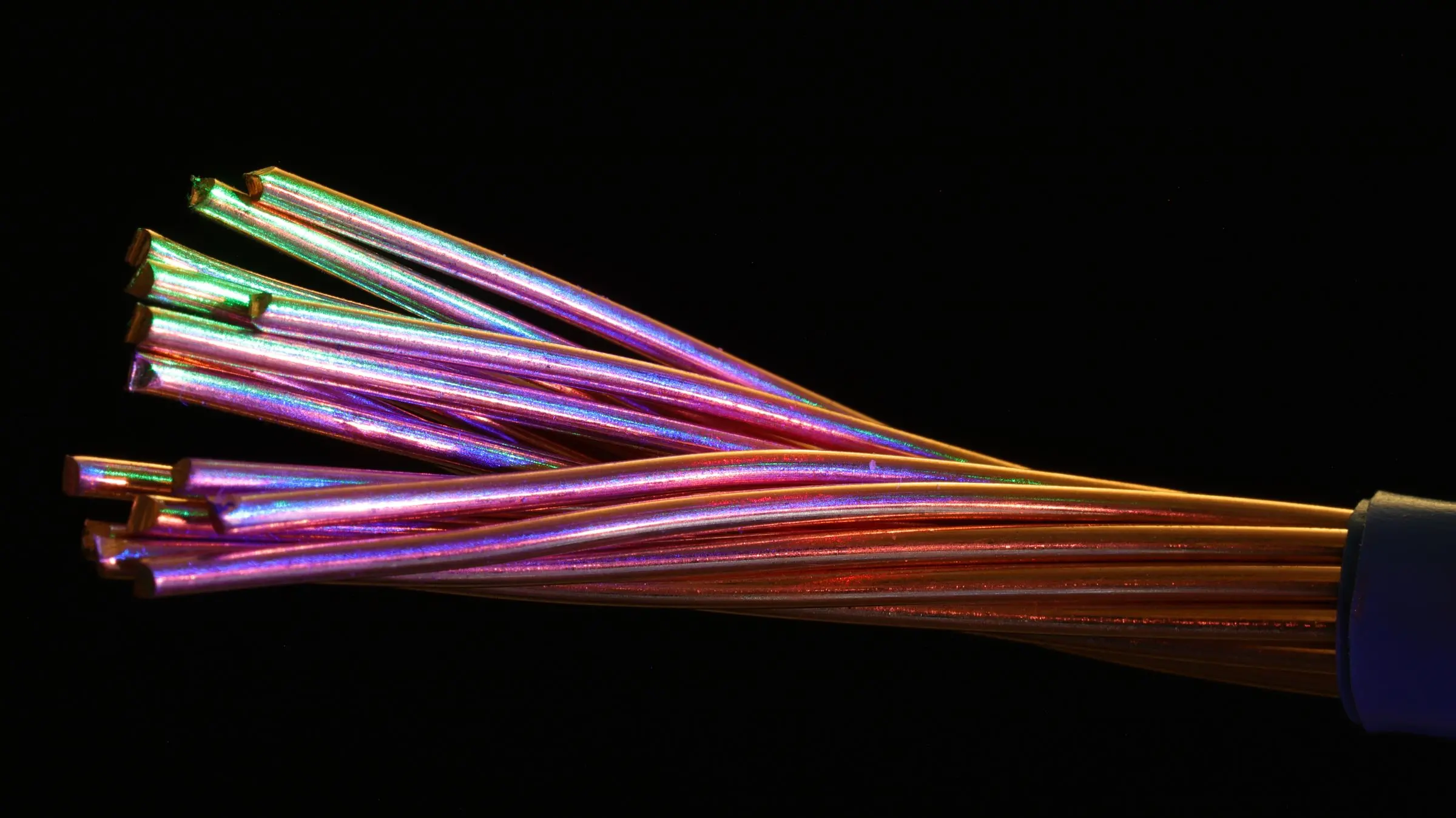 Un trefolo di rame spellato che si apre a ventaglio su fondo nero, con riflessi iridescenti