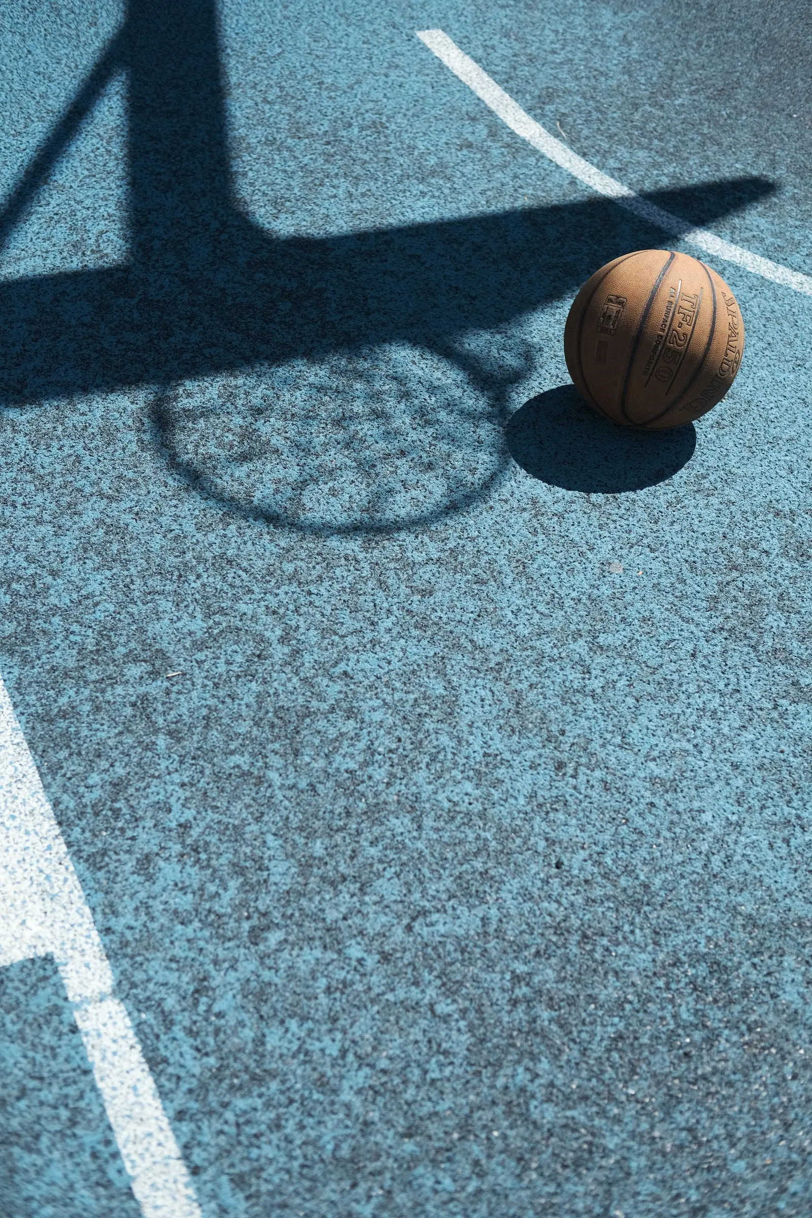 Pallone da basket su un campo azzurro, accanto all'ombra del canestro