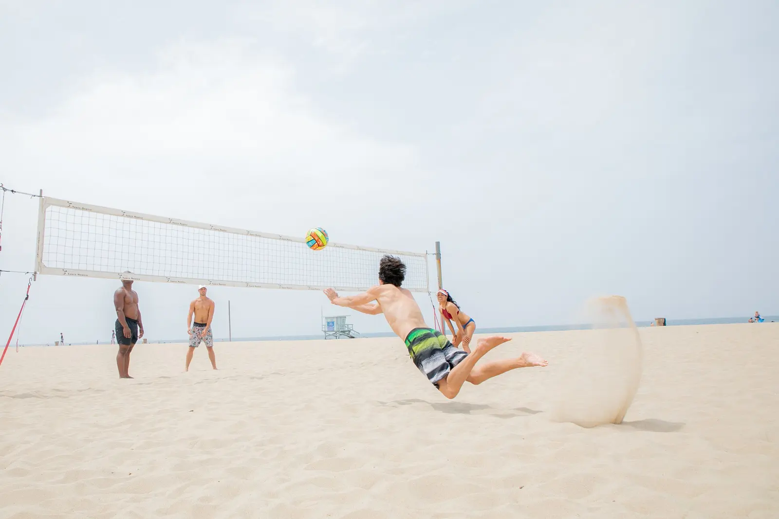 Tuffo sulla sabbia per prendere la palla sotto rete, in una partita di beach volley