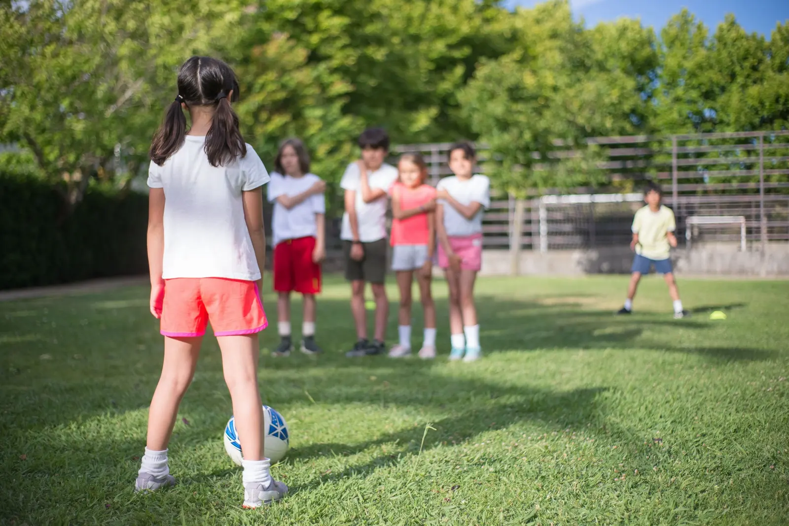 Bambini in fila sul prato aspettano il proprio turno per calciare il pallone