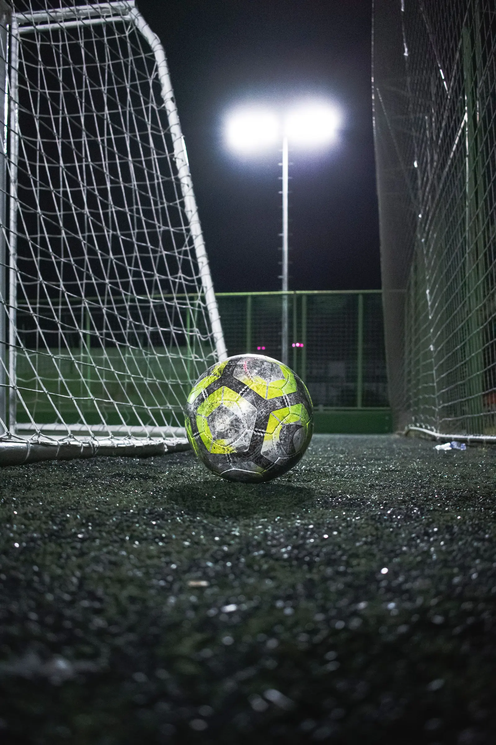 Pallone fermo davanti alla porta di calcetto, di notte, con il faro acceso dietro la rete