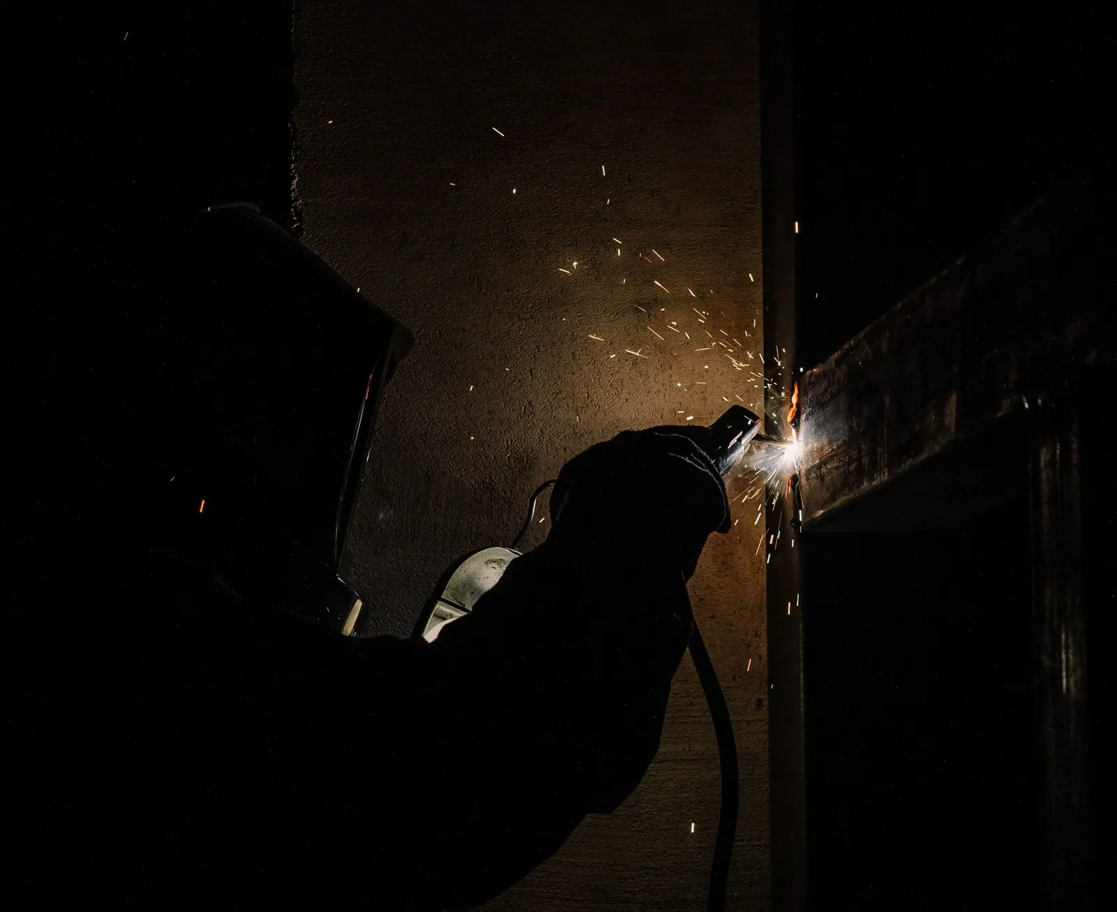 Saldatore al lavoro nell'officina, nel buio, tra le scintille