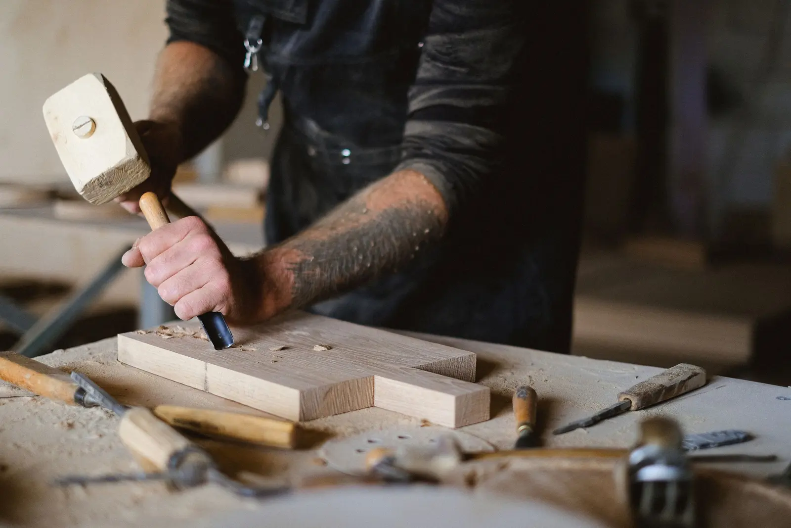 Mani di un falegname che lavorano il legno con mazzuolo e scalpello