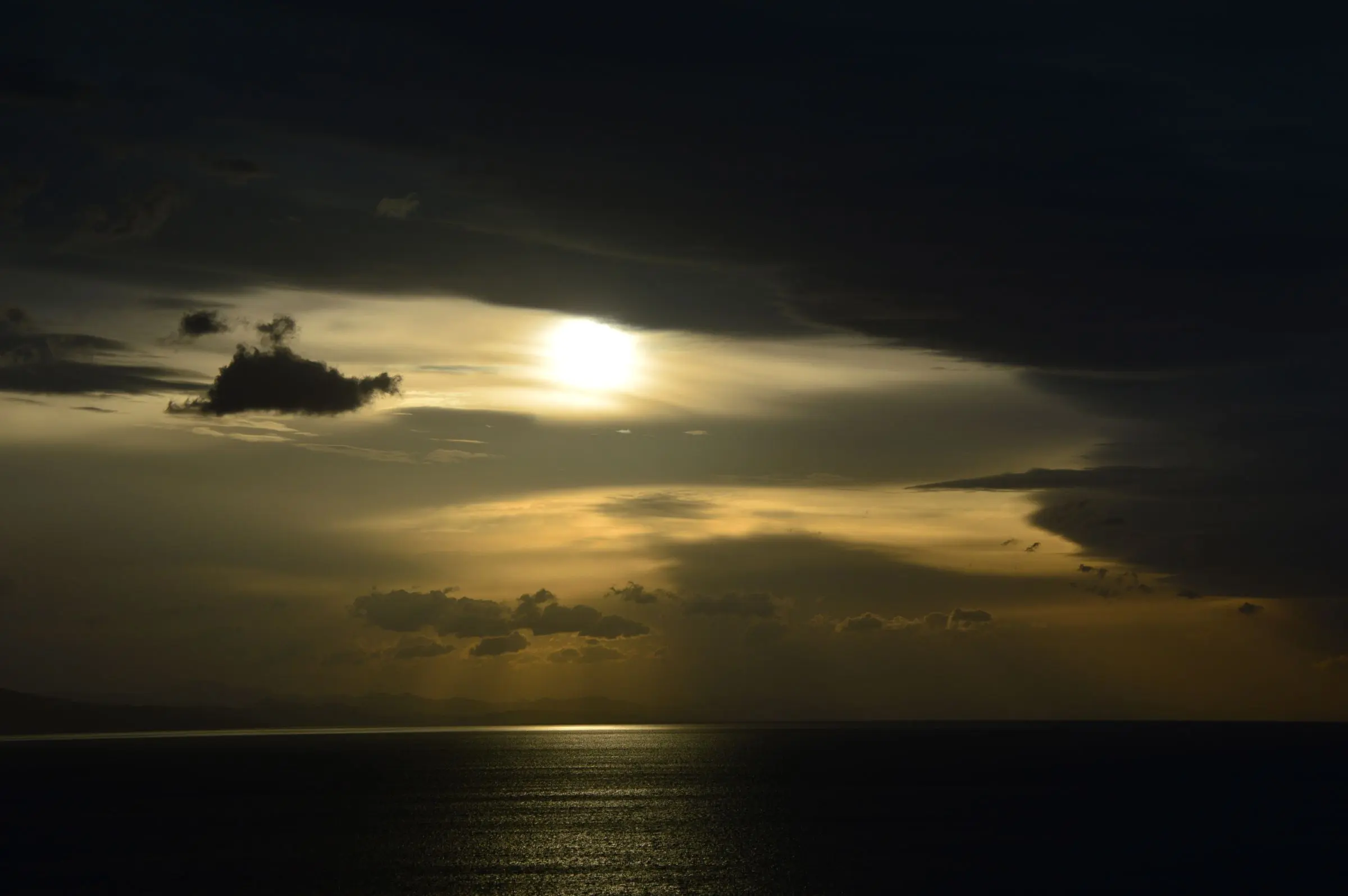 Cielo scuro sul mare aperto al tramonto, con il sole velato dalle nuvole