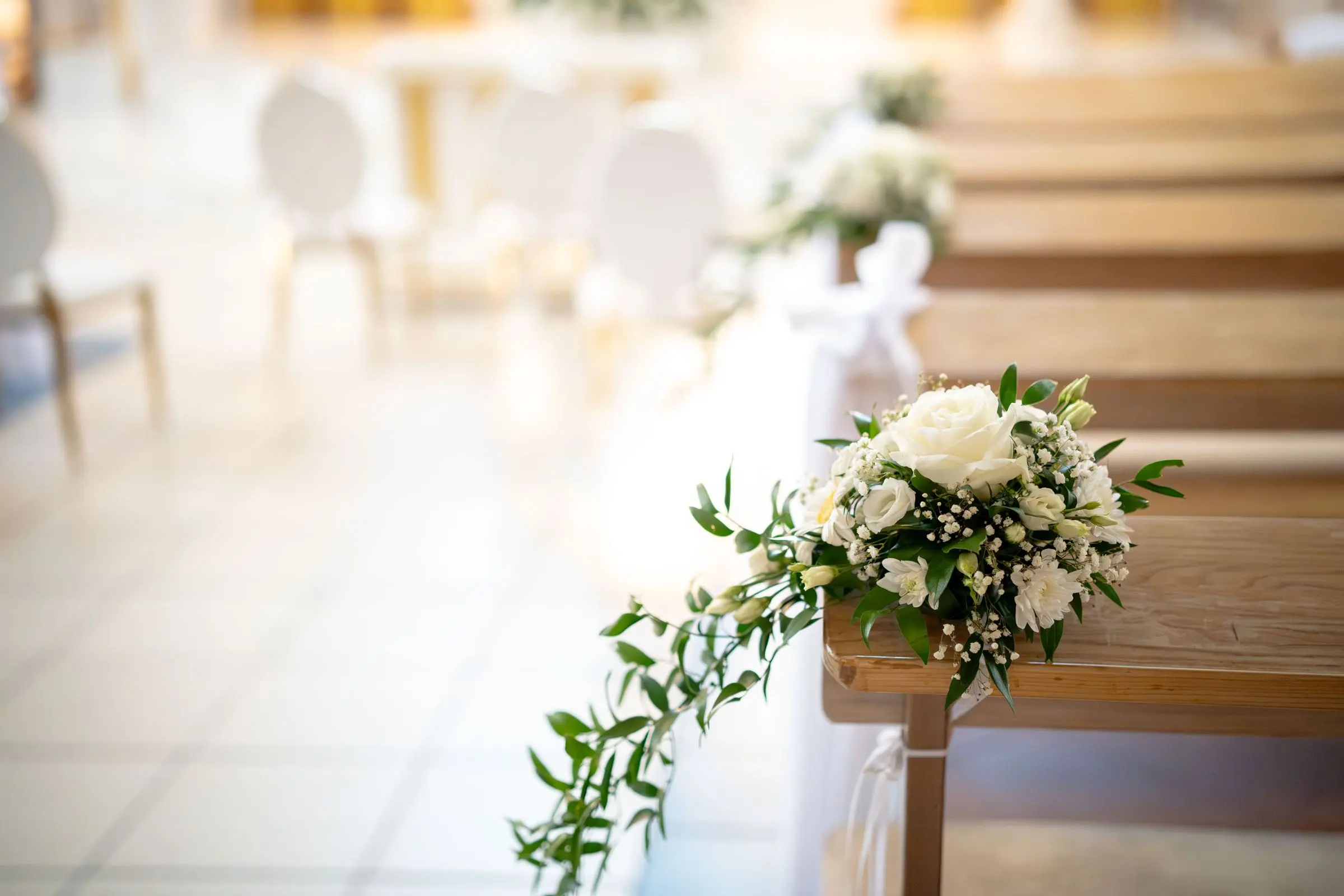 Rose bianche ed edera legate alle panche di una navata, in una luce chiara