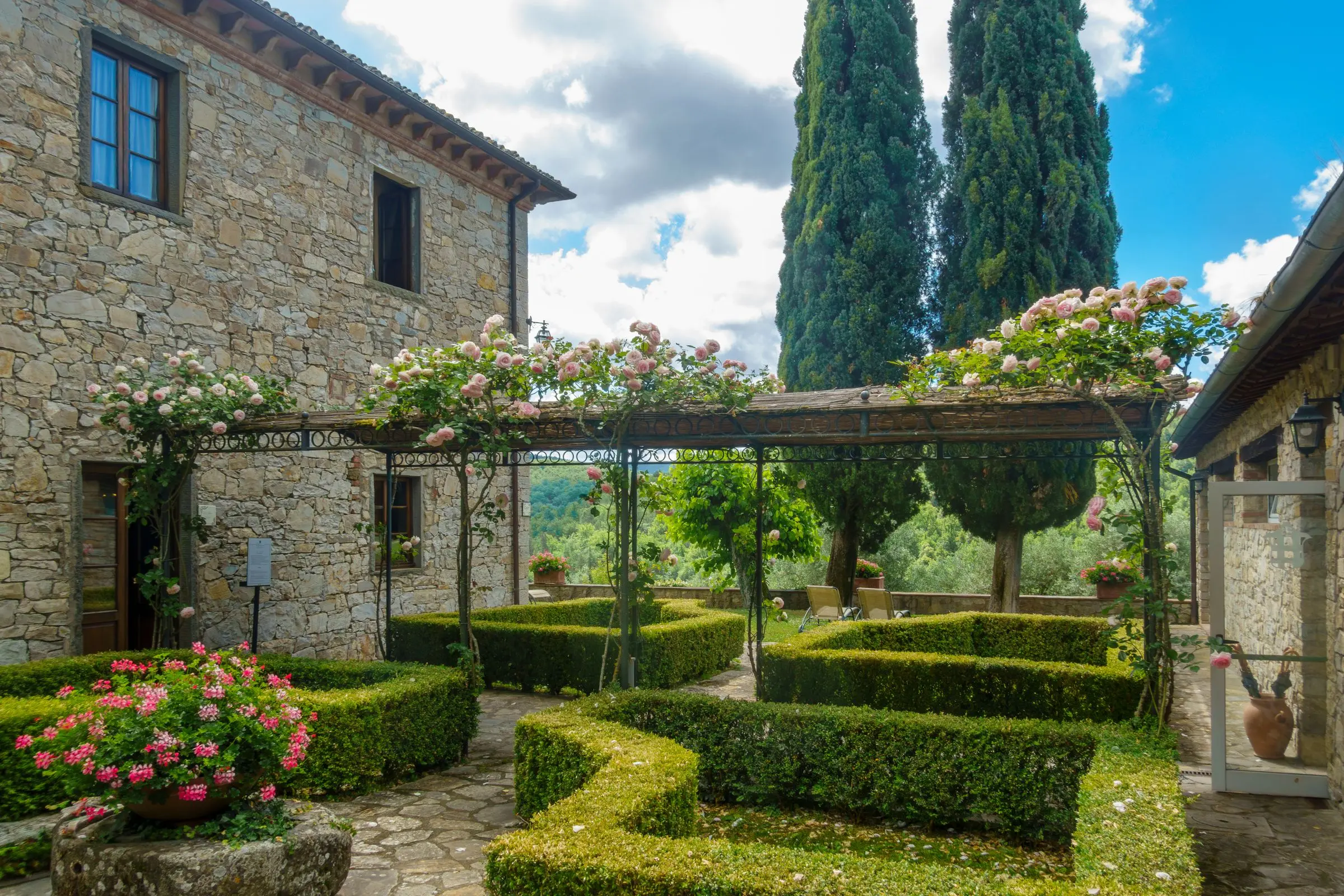 Giardino all'italiana con siepi di bosso, rose in fiore e un pergolato in pietra
