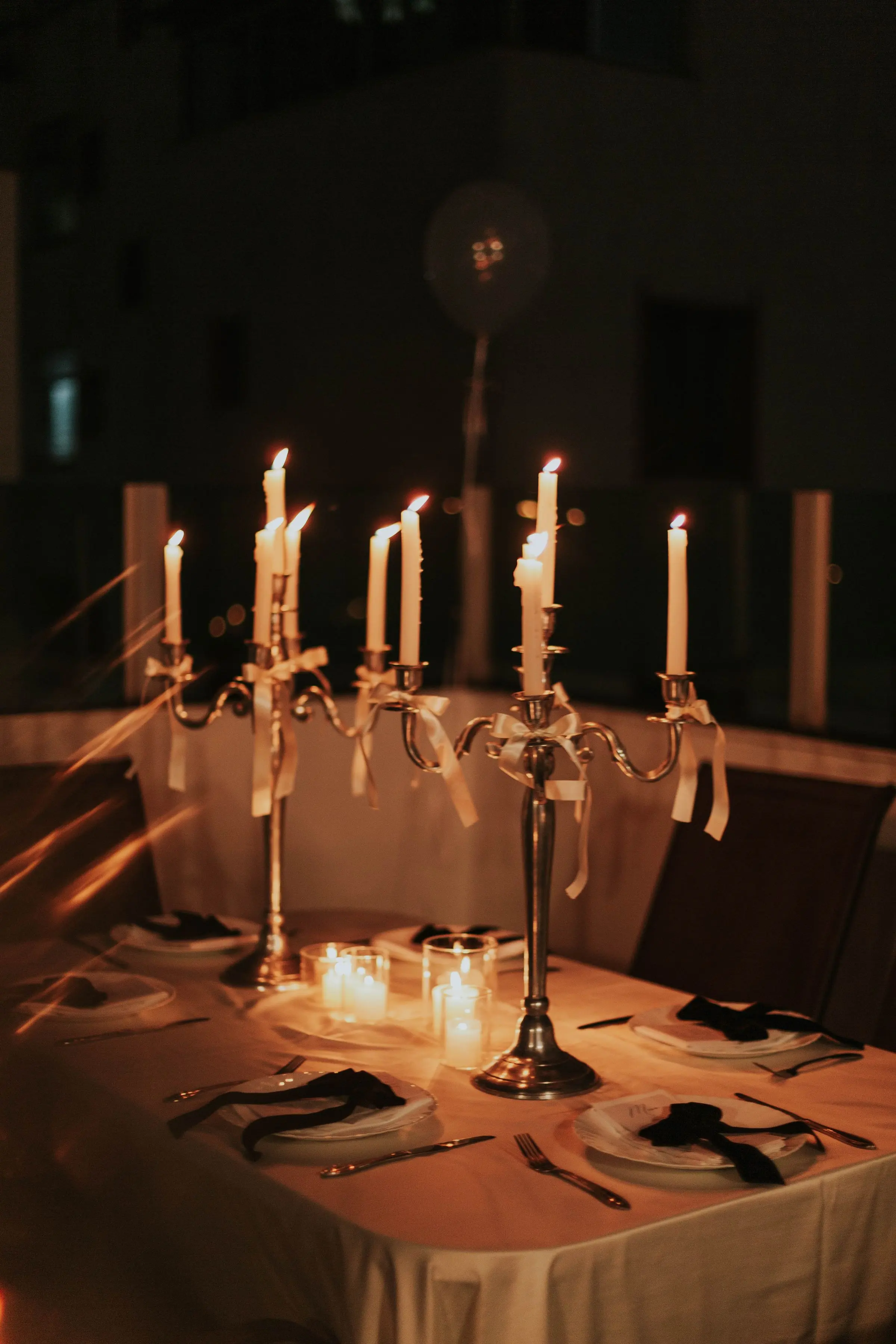 Candelabri d'argento accesi su una tovaglia bianca, la sala intorno al buio