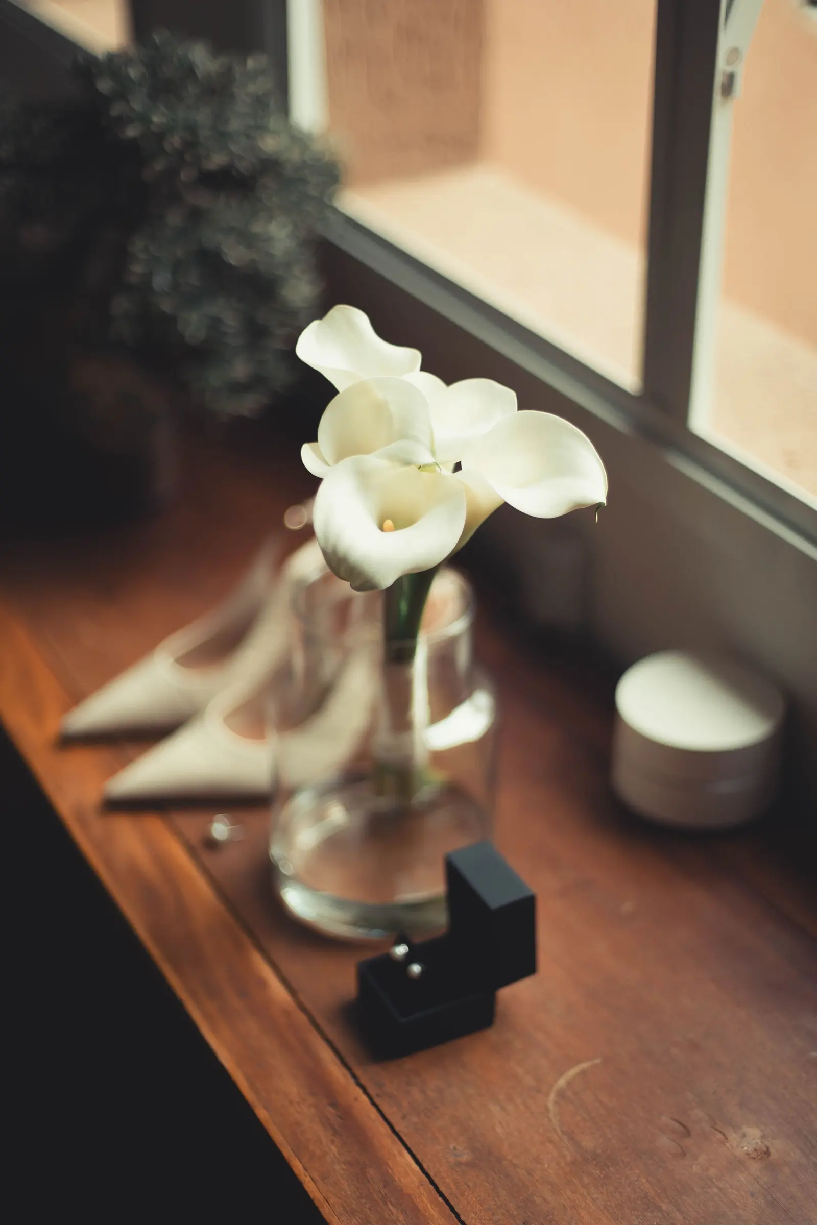 Una calla bianca in un vaso di vetro su un davanzale, accanto alle scarpe e alla scatola degli anelli