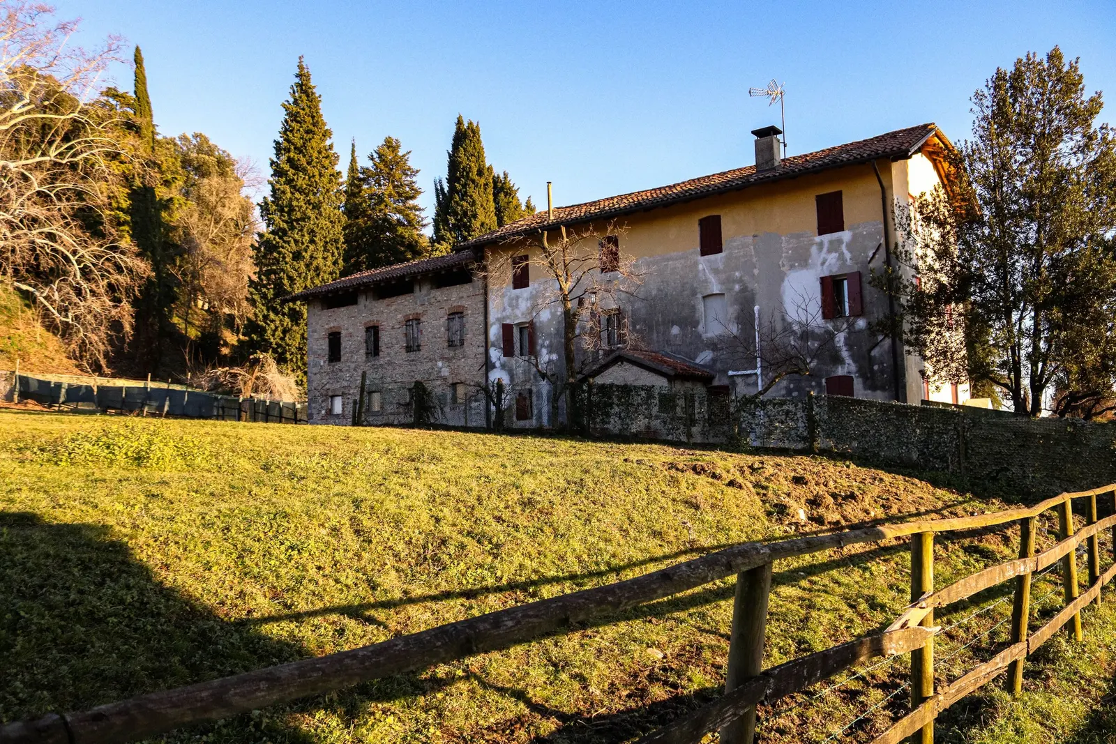 Casale in pietra con la staccionata di legno e il prato al sole