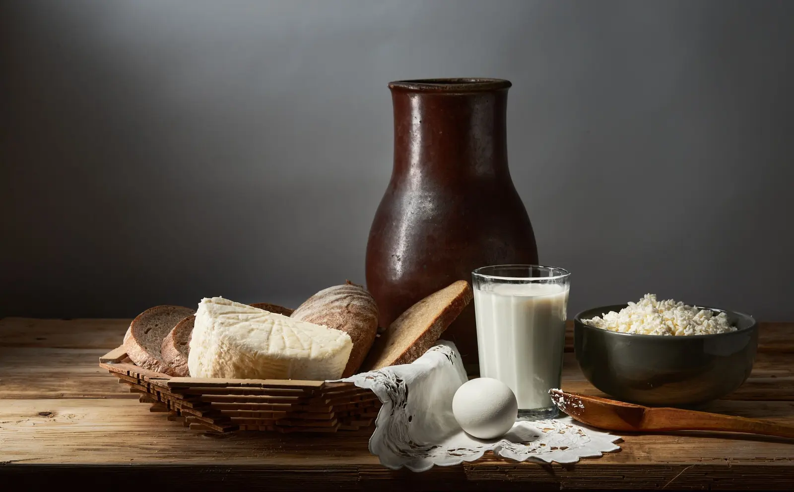 Brocca di terracotta, latte, ricotta, pane e uova su un tavolo di legno
