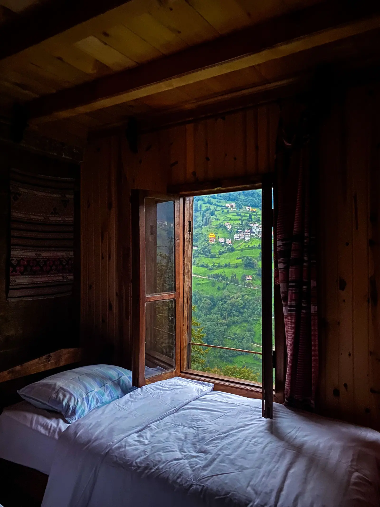 Camera con pareti di legno e una finestra aperta sulle colline verdi