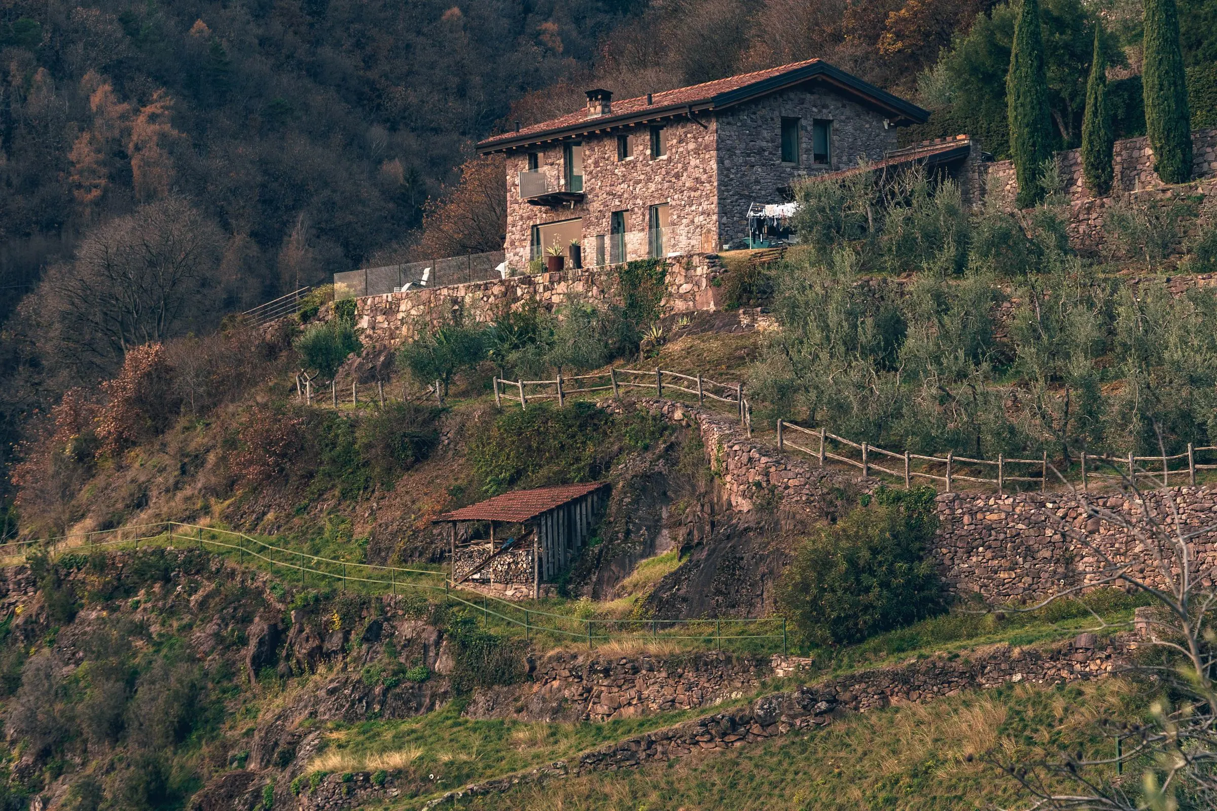 Casale di pietra su un colle in autunno, con i terrazzamenti e il bosco intorno